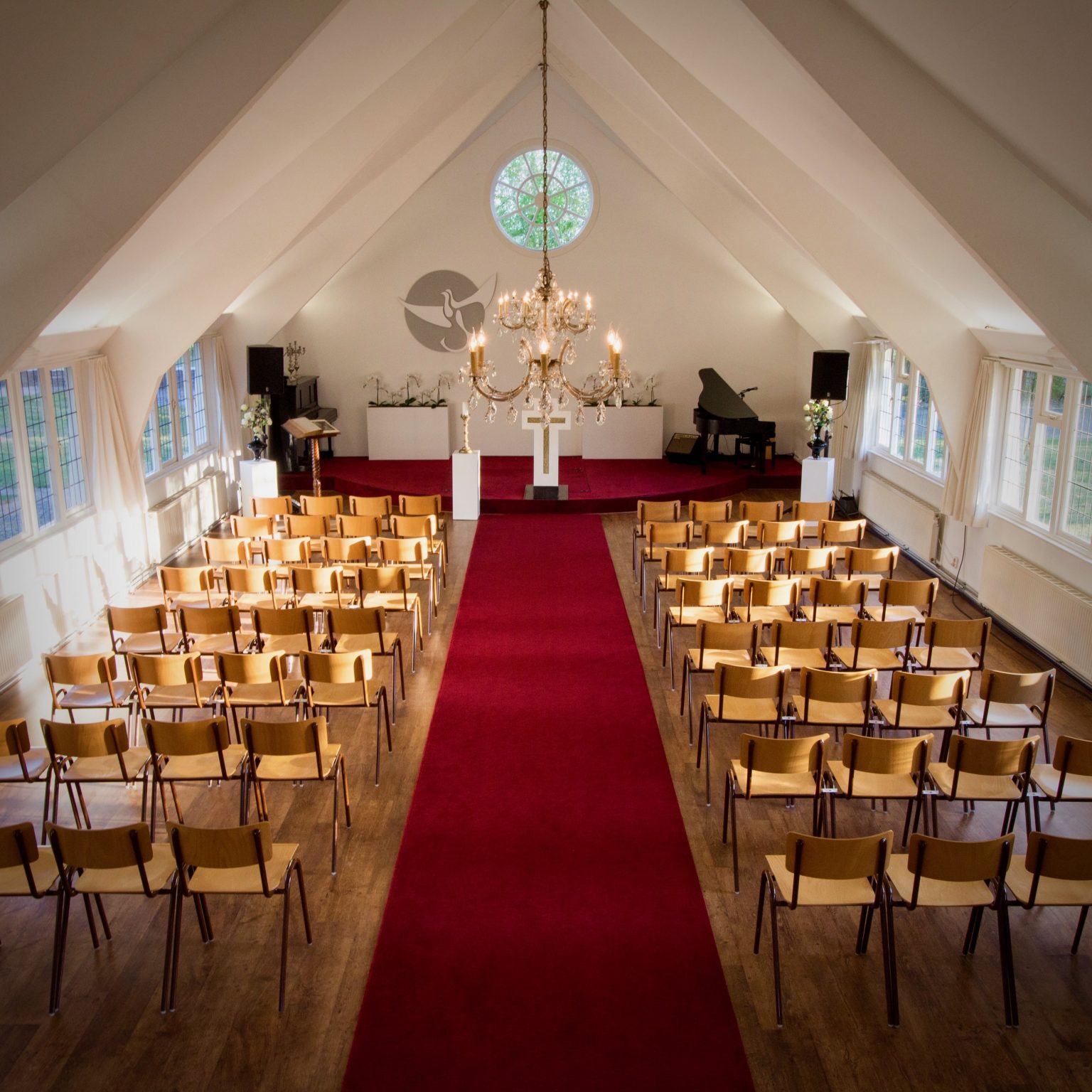 Interieur van het Wit Kerkje met rode loper, kroonluchter, vleugelpiano en karakteristieke houten stoelen - ceremonie ruimte voor bruiloften en uitvaarten